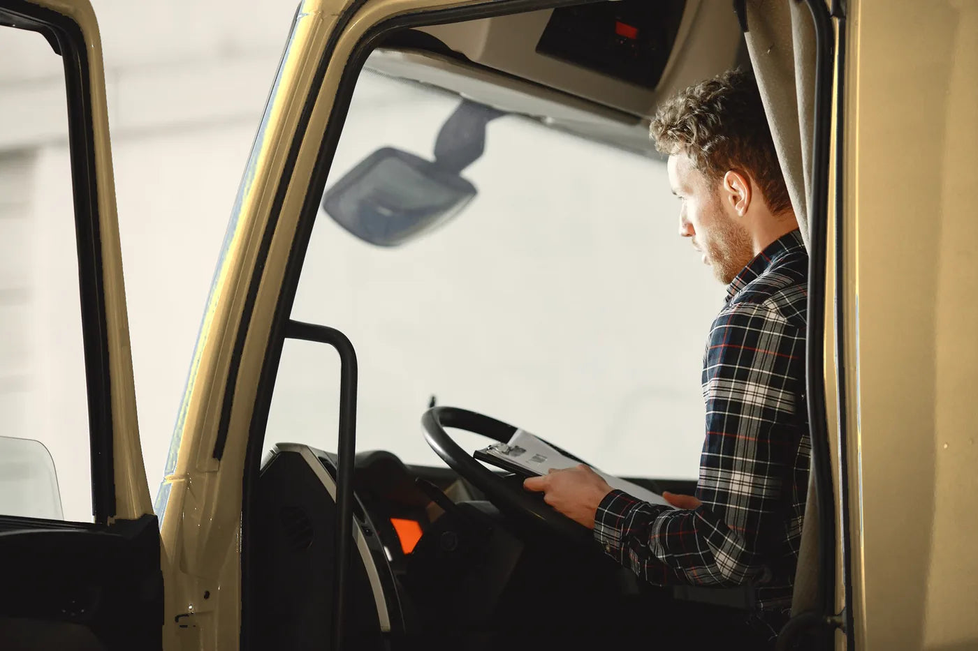 Lkw-Fahrer mit Lieferpapieren im Fahrerhaus eines beigefarbenen Lkw